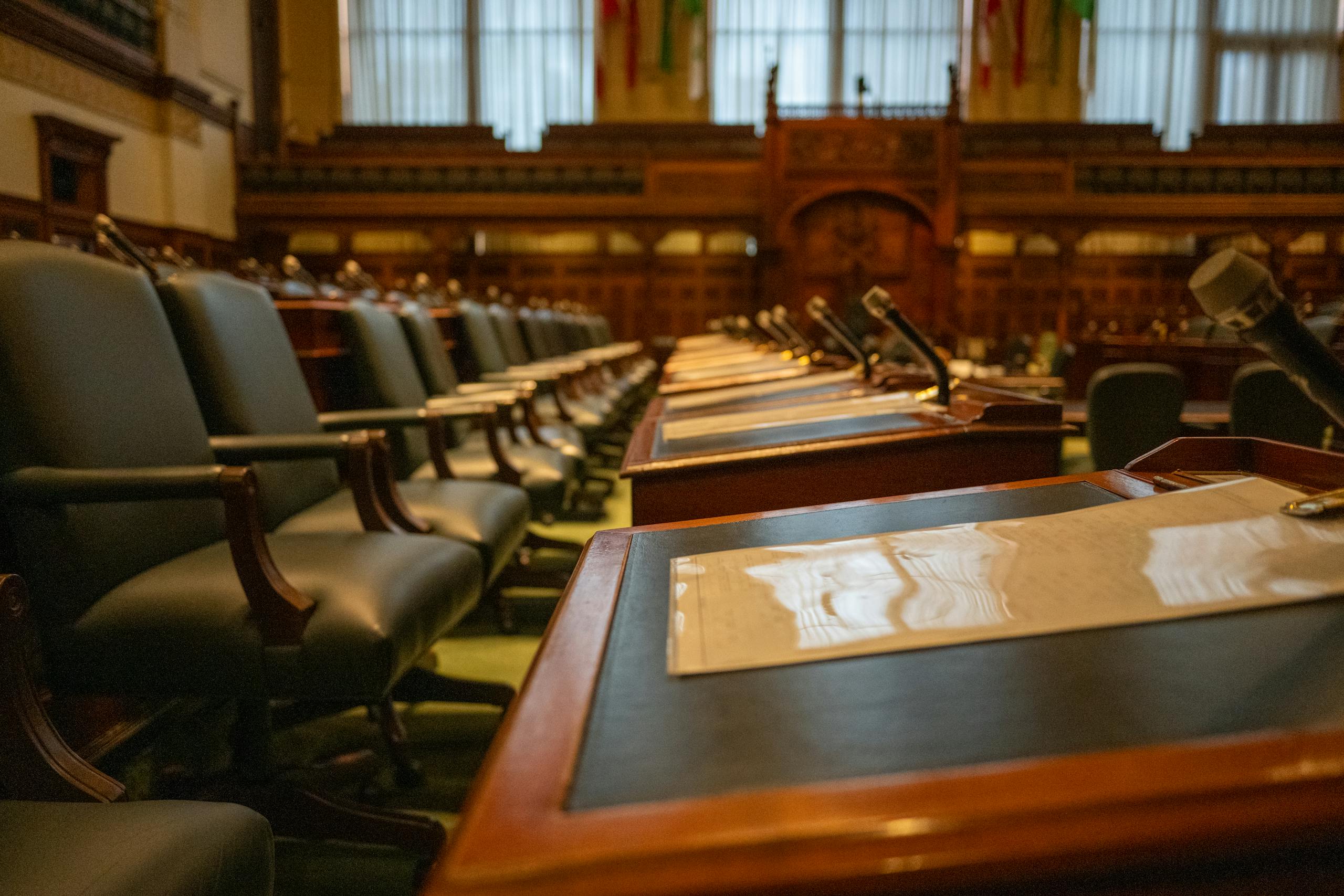 A detailed view of an empty legislative chamber with rows of desks and microphones, evoking governance.