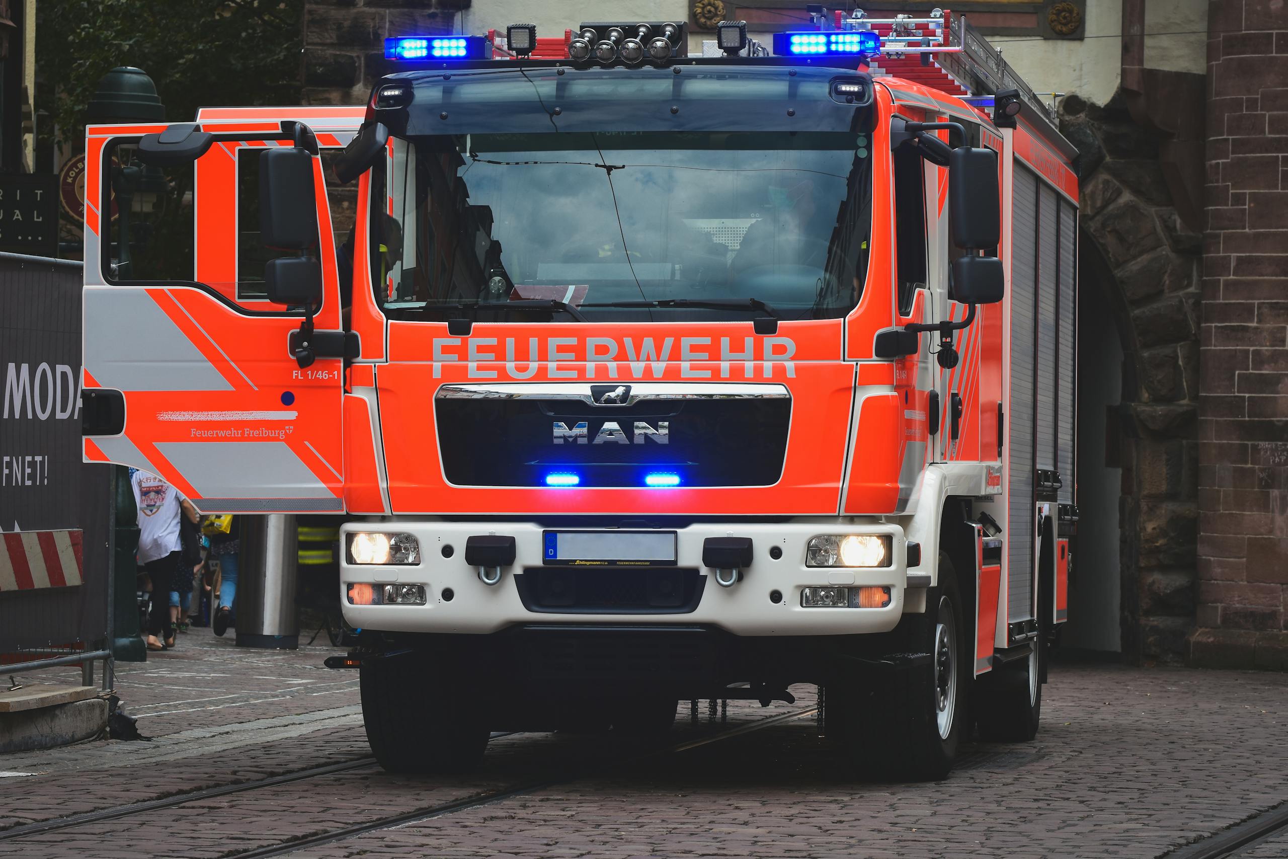 Bright red fire truck with blue lights on a city street in daylight.